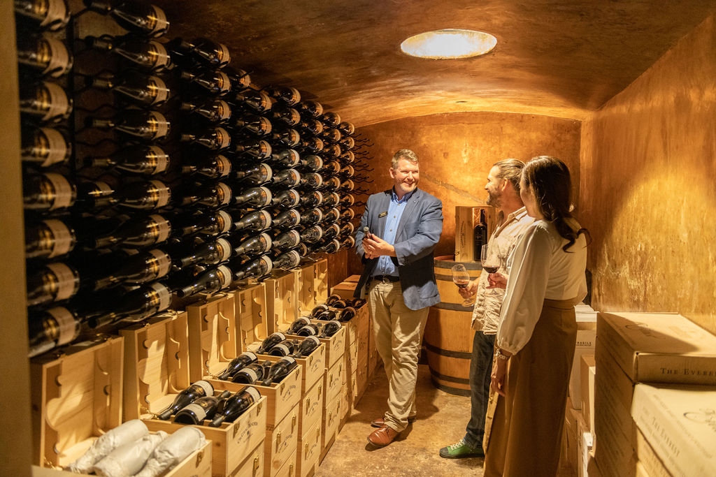 A man giving a tour of wine cellar to a man and a woman